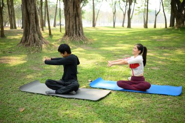 Erkek ve kadın, açık hava parkında yoga minderleri üzerinde egzersiz yapıyorlar..