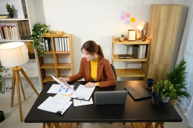 Gülümseyen genç girişimci modern ofis çalışma alanındaki haritaları ve verileri inceliyor.