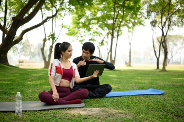 Kişisel antrenör ve istemci parkta bir açık hava fitness oturumu sırasında dijital tablet üzerinde çalışma planı gözden geçiriyorlar.