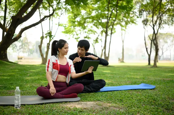 Kişisel antrenör ve istemci parkta bir açık hava fitness oturumu sırasında dijital tablet üzerinde çalışma planı gözden geçiriyorlar.