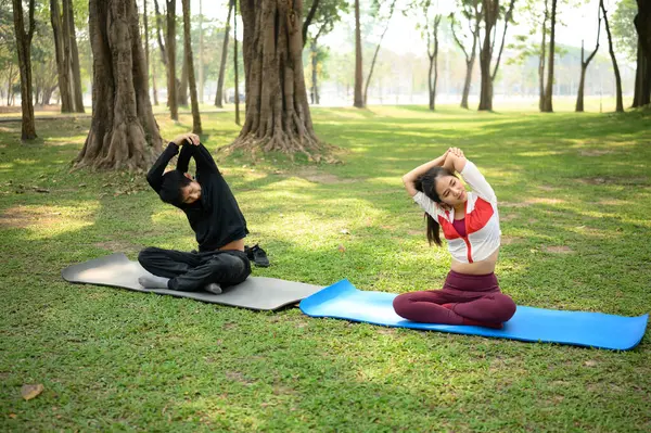 Genç çift sabah yoga seansı boyunca parkta çimenli bir zeminde esniyorlar..