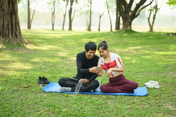 Yeşil bir parkta oturmuş spor salonlarından sonra cep telefonlarını kontrol eden mutlu bir çift..