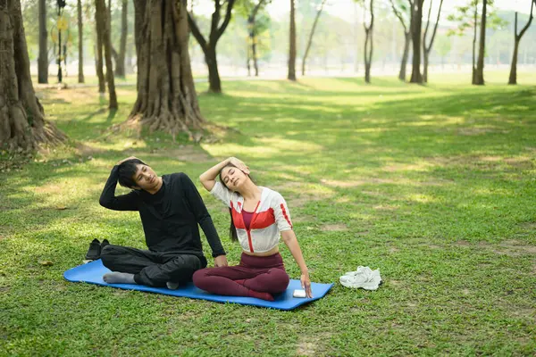 Erkek ve kadın sabah yoga seansı boyunca parkta çimenli bir zeminde esniyorlar..