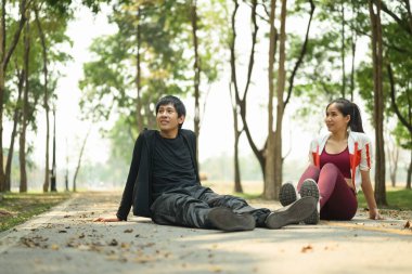 Genç bir çift parkta oturmuş egzersiz yaptıktan sonra sakin bir anın tadını çıkarıyor..