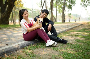 Köpekleri ile kaldırımda oturan mutlu genç çift güneşli bir parkta antrenmandan sonra dinleniyorlar..