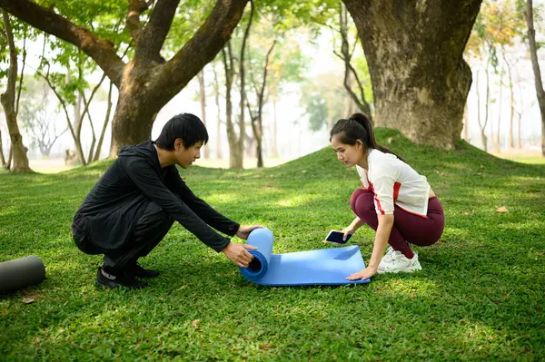 Aktif çift yemyeşil çimenlikte yoga minderini açıyor, birlikte spor salonuna hazırlanıyorlar..