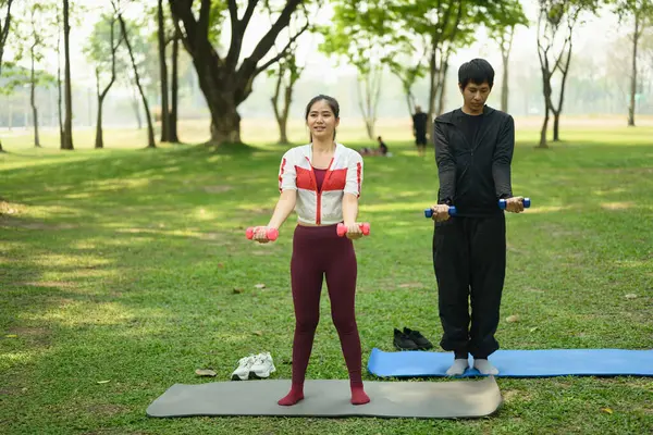 Genç çift, huzurlu bir parkta dambıllarıyla egzersiz yapıyor. Sağlık ve sağlıklı yaşam tarzı kavramı.