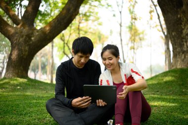 Aktif kıyafetli Asyalı çift antrenmandan sonra dinleniyor ve tablet izliyor..