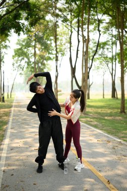 Genç ve zinde bir çift parkta egzersiz yapmadan önce esneme hareketleri yapıyor..