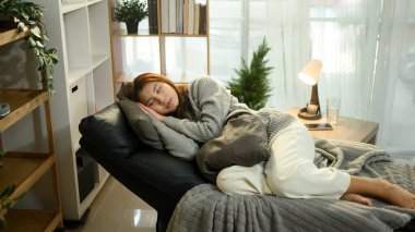 Genç bir kadın rahat bir oturma odasında koltukta rahatça kestiriyor..