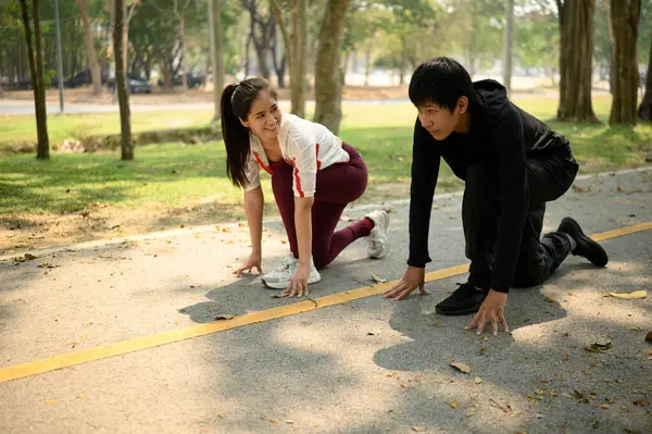 Genç çift parkta koşmaya hazırlanıyor, bir patikada başlangıç pozisyonunda çömelmiş..