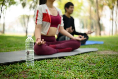 Arka planda yoga minderleri üzerinde meditasyon yapan bir çiftin olduğu su şişesini kapat..