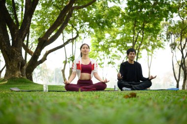 Genç bir çift, huzurlu bir parkta farkındalık meditasyonu yapıyor. Zihinsel sağlık konsepti.