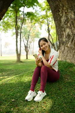 Antrenmandan sonra kablosuz kulaklıkla akıllı telefonunu kullanan gülümseyen kadın..