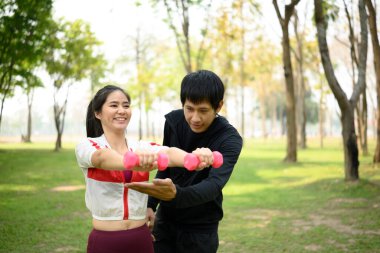 Yeşil bir parkta dambıllarla egzersiz yapan aktif bir erkek ve kadın..