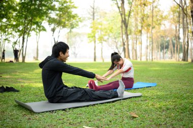 Genç bir adam ve kadın yeşil bir parkta yoga minderleri üzerinde birlikte esniyorlar. Sağlıklı yaşam tarzı kavramı.