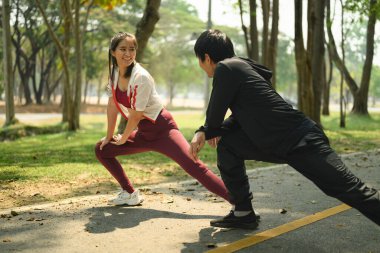 Güneşli bir park yolunda koşmadan önce birlikte gerinen atletik çift.