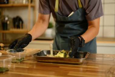 Siyah eldivenli bir adam mutfak tezgahında tereyağıyla taze otları ve sarımsağı karıştırıyor..