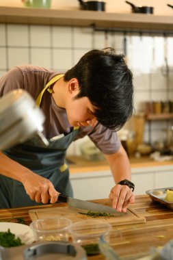 Odaklanmış bir adam tereyağı için tahta kesme tahtasının üzerinde taze otlar kesiyor..