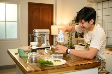 Önlüklü genç adam, kremayla karıştırıcıyı paslanmaz çelik bir kasede karıştırıyor..