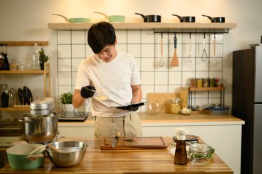 Gülümseyen Asyalı adam krem şanti hazırlarken dijital tablette bir tarifi takip ediyor..