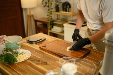 Modern bir mutfağın tahta kesme tahtasıyla sarımsak doğrayan adama yakın çekim..