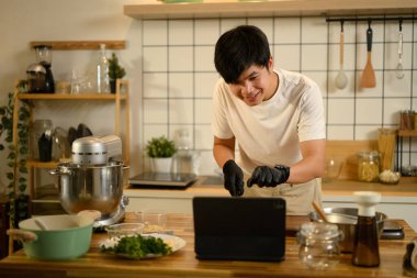 Gülümseyen Asyalı adam krem şanti hazırlarken dijital tablette bir tarifi takip ediyor..