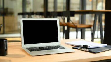 Boş ekranlı dizüstü bilgisayar, finansal döküman ve ahşap masada kahve fincanı..