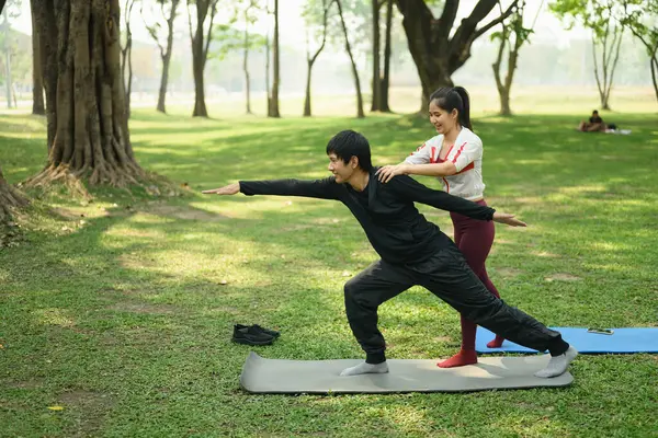 Parkta birlikte yoga yapan mutlu genç çift. Sağlıklı yaşam ve farkındalık kavramı.