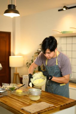 Ev mutfağında tereyağını ayırmak için taze tereyağını süzgece döken adam..