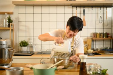 Gülümseyen Asyalı adam paslanmaz çelik kasede krema çırpmak için el bilgisayarı kullanıyor..