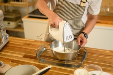 Gülümseyen Asyalı adam paslanmaz çelik kasede krema çırpmak için el bilgisayarı kullanıyor..