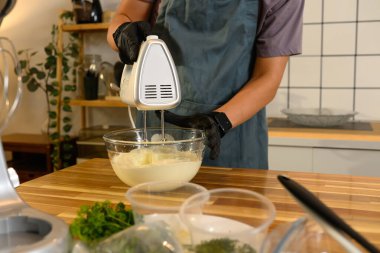 Siyah eldivenli adam cam kasede kremayla elektrikli el mikserini karıştırıyor..