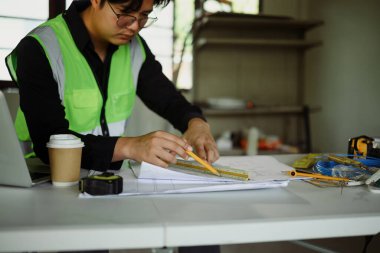 İşlek bir çalışma alanındaki ölçüm araçlarıyla bina planlarını gözden geçiren mimar.