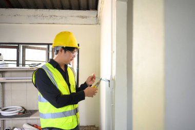 Sarı şapkalı elektrikçi inşaat alanındaki elektrik tesisatında çalışıyor..