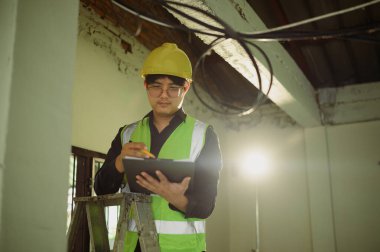 Profesyonel elektrikçi planlarını gözden geçirir ve elektrik denetimi yaparken notlar alır..