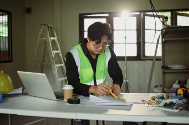 İşlek bir çalışma alanındaki ölçüm araçlarıyla bina planlarını gözden geçiren mimar.