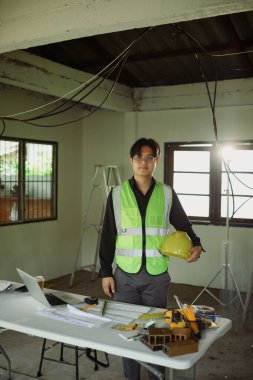 İnşaat alanında sarı şapka tutan güvenlik yeleği giymiş bir mühendis..