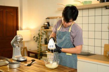 Siyah eldivenli adam cam kasede kremayla elektrikli el mikserini karıştırıyor..