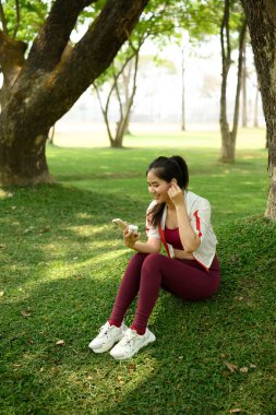 Antrenmandan sonra kablosuz kulaklıkla akıllı telefonunu kullanan gülümseyen kadın..