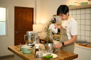 Önlüklü genç adam, kremayla karıştırıcıyı paslanmaz çelik bir kasede karıştırıyor..