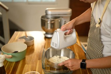 Önlüklü genç adam, kremayla karıştırıcıyı paslanmaz çelik bir kasede karıştırıyor..