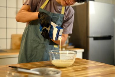 Önlüklü ve eldivenli bir adam tereyağı yapmak için cam bir kaseye ağır krema döküyor..