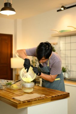 Ev mutfağında tereyağını ayırmak için taze tereyağını süzgece döken adam..