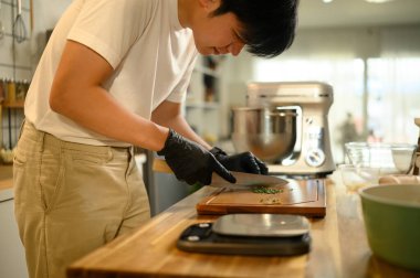 Siyah eldivenli bir adam tahta kesme tahtasına otları kesiyor..