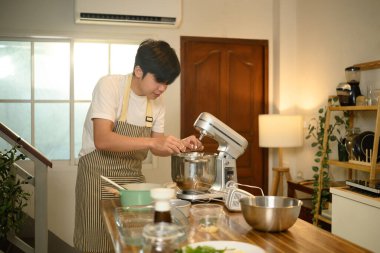 Önlük takan genç adam çırpılmış kremayı karıştırma kabına malzemeler ekleyerek hazırlıyor..