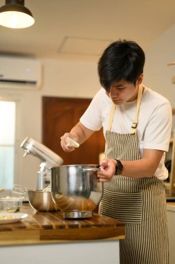 Önlük takan genç adam çırpılmış kremayı karıştırma kabına malzemeler ekleyerek hazırlıyor..