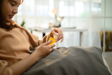 Kanepede dinlenirken günlük giysiler içinde ilaç alan Asyalı genç bir kadın..