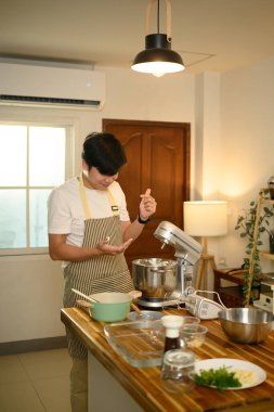 Genç Asyalı adam modern bir mutfakta krema çırpmak için karıştırıcı kullanıyor..