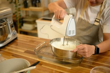 Adam ev yapımı pişirme seansı sırasında paslanmaz çelik kasede kremayla elektrikli çırpıcıyı karıştırıyor..